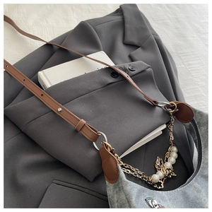 Detail of blue denim shoulder bag with pearl metal chain on grey blazer background