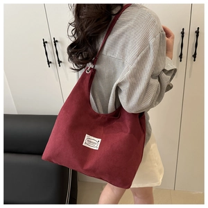 Detail of burgundy corduroy tote bag featuring a white fashion label and silver buckles