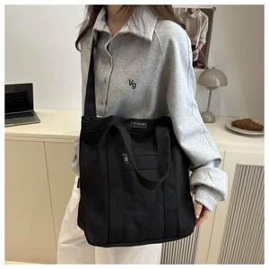 Détail du sac cabas noir en toile avec étiquette tendance et poche zippée à l'avant