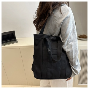 Détail d'un grand sac cabas en toile noire montrant l'étiquette mode et la bandoulière