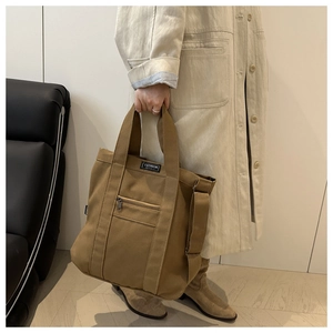 Detail of dark camel canvas tote bag featuring front zip pocket and fashion patch