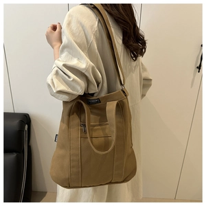 Détail du sac cabas en toile camel montrant la poche zippée extérieure et l'étiquette mode
