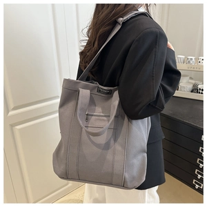 Vue latérale du grand sac cabas en toile grise avec bandoulière réglable et poche avant