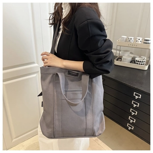 Détail du sac seau en toile grise avec étiquette mode et poche avant zippée