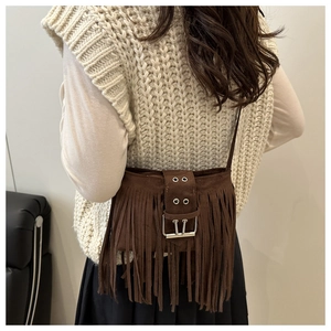 Detail of dark brown suede crossbody bag with fringe accents and silver metal buckle