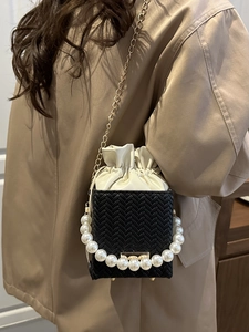 Fashionable black woven bucket bag with pearl handle and gold chain strap shown on a model