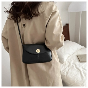 Detail of a black leather crossbody bag featuring a golden circular twist lock on a beige coat
