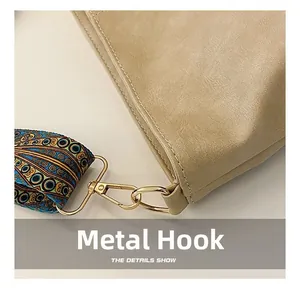 Close-up of golden hardware hook and geometric pattern strap on beige leather bucket bag