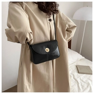 Detail of a black leather crossbody bag with a round gold metal twist lock on a beige coat