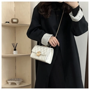 Détail d'un sac bandoulière blanc matelassé avec fermoir doré porté sur un manteau noir