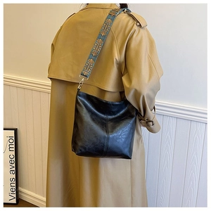 Detail of black hobo bag with a blue vintage patterned wide jacquard strap on a beige trench coat