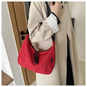 Detail of red nylon shoulder bag featuring black wide strap and thick woven zipper pull