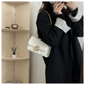 Détail d'un sac à main blanc matelassé avec fermoir doré rotatif et bandoulière chaîne