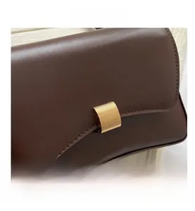 Detail of dark brown leather bag showing gold striped metal lock and smooth texture