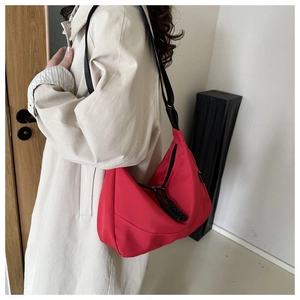 Detail of red nylon crescent bag with adjustable wide black strap on beige coat