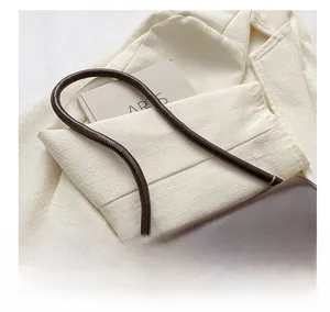 Detailed close-up of dark brown leather shoulder bag with gold metal buckle on tweed blazer