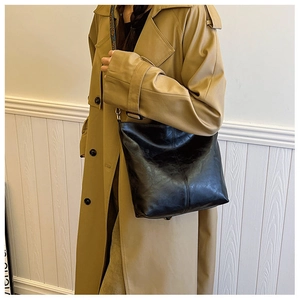 Detail showing the glossy synthetic leather texture and stitching of the black tote bag