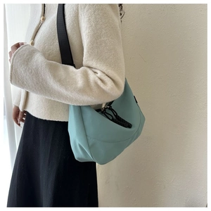 Detail view of a light blue nylon crescent bag with a wide black strap and zipper pull