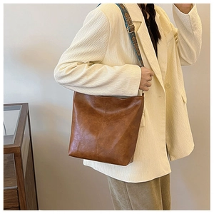 Brown leather bucket bag with retro jacquard strap details on a beige blazer background