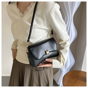 Detailed side view of black leather shoulder bag with gold metal buckle and thin strap