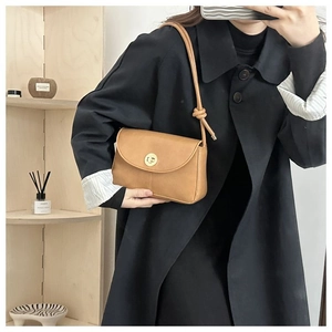 Close-up of camel leather shoulder bag with a gold twist lock and knot detail strap