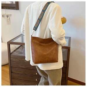 Detail of a brown leather bucket bag with an ethnic style embroidered wide shoulder strap