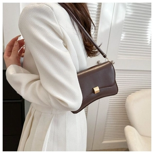 Detail of a dark brown leather baguette bag featuring a minimalist golden metal buckle