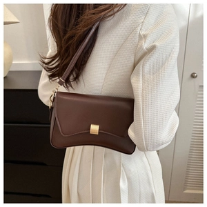 Close-up of a dark coffee baguette bag with gold buckle on a tweed jacket