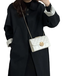 Sac à bandoulière matelassé blanc avec chaîne dorée porté sur un long manteau noir chic