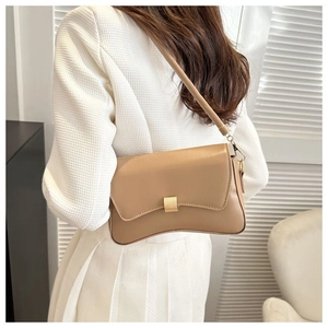 Detail view of the elegant curved bottom and golden lock of this beige baguette bag