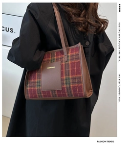 Detail of plaid tote bag with leather logo patch worn on shoulder by model