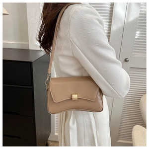Side view of beige leather baguette bag on model showing metal buckle and curved base