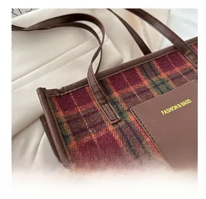 Detail of plaid tote bag featuring checkered fabric and leather pocket with fashion text