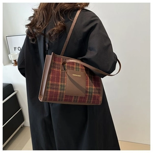 Detail of red and green plaid tote bag with brown leather strap worn over a black coat