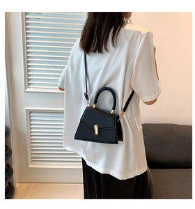 Détail d'un mini sac trapèze noir avec boucles dorées porté en sac bandoulière chic