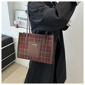 Detail of red and green plaid tote bag with brown leather patch and dual handles