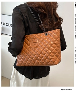 Close-up of brown quilted tote bag with metal chain strap and embossed logo detail
