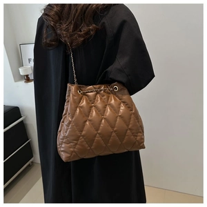 Detail of dark brown quilted bucket bag featuring gold chain strap and drawstring closure