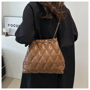 Detail of a brown quilted leather bucket bag with gold chain strap on a black coat