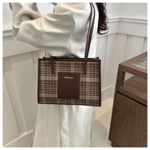 Close-up of vintage plaid tote bag featuring brown leather straps and tweed texture