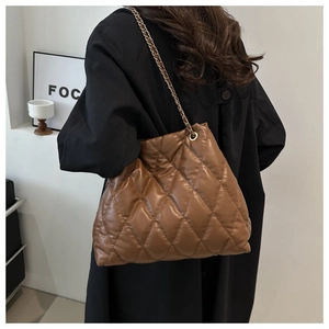 Close-up of quilted caramel brown bucket bag with gold chain strap on model shoulder