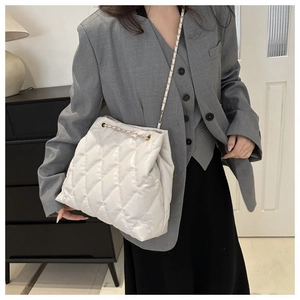 Detailed view of white quilted bucket bag with chain strap worn with grey blazer