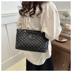Detail of black quilted tote bag with silver chain strap and metal logo on smooth leather