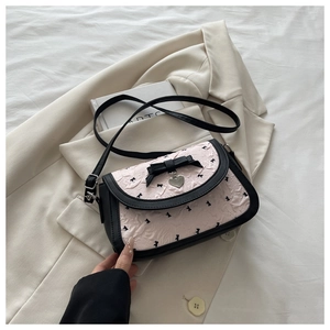 Detail of pink bow-knot handbag with black leather trim and heart pendant over a beige coat