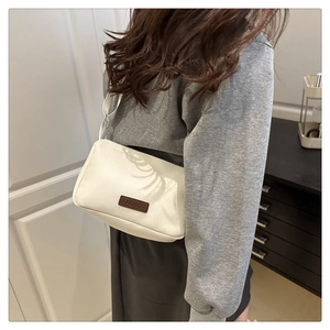 Close-up of beige square crossbody bag with brown FASHION tag and adjustable strap