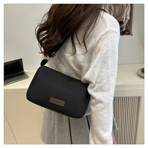 Rear view of a stylish black nylon crossbody bag on a model in a minimalist workspace