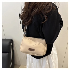 Détail du sac bandoulière en toile beige avec étiquette en cuir marron sur le modèle