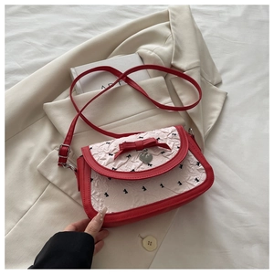 Detail of red and white crossbody bag featuring bow embroidery and heart pendant