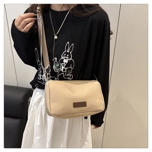 Detail of beige canvas crossbody bag with brown leather logo patch and wide strap