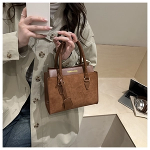 Détail du sac à main vintage en daim marron avec doubles anses et finitions dorées mat
